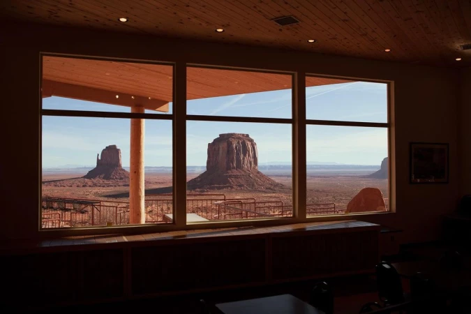 Monument Valley view framed by large window in building. Desert landscape with rock formations visible during daytime.