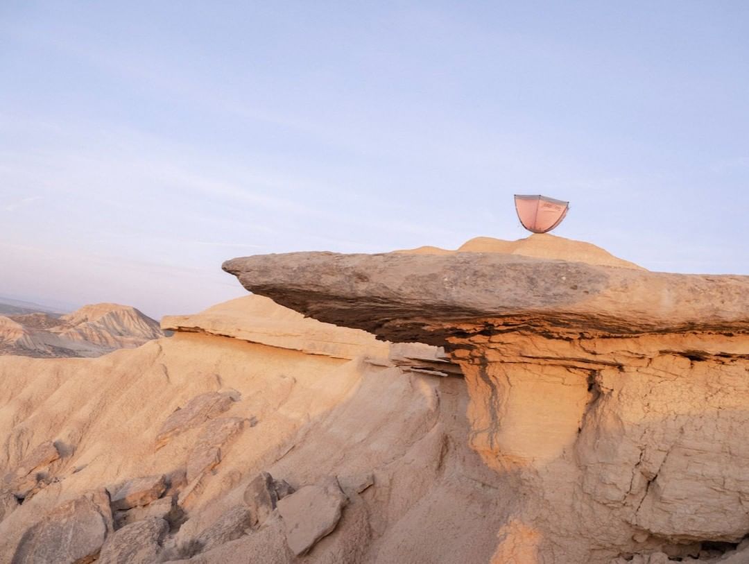 Desert landscape features rock formations and a small decorative sculpture, set under a pastel sky at either dawn or dusk.