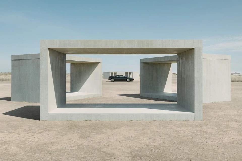 Vintage car parked in the distance, framed by concrete geometric structures in a desert landscape under a clear blue sky. Automotive photography.