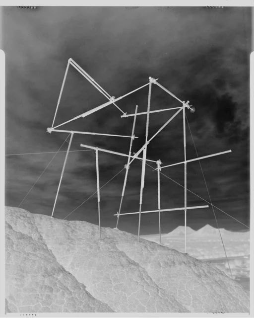 Abstract construction on a rocky hill under a cloudy sky. Complex geometric scaffolding structure contrasts with the natural landscape.