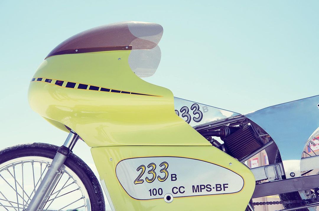 Close-up of a vintage racing motorcycle with a yellow fairing, set against a clear blue sky, showcasing its unique design and aerodynamic features.