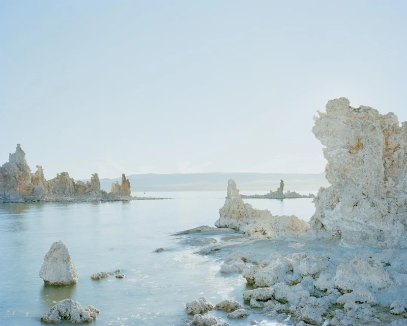 Tufa rock formations rising from the tranquil waters of Mono Lake, California, bathed in soft, diffused light and clear blue sky.