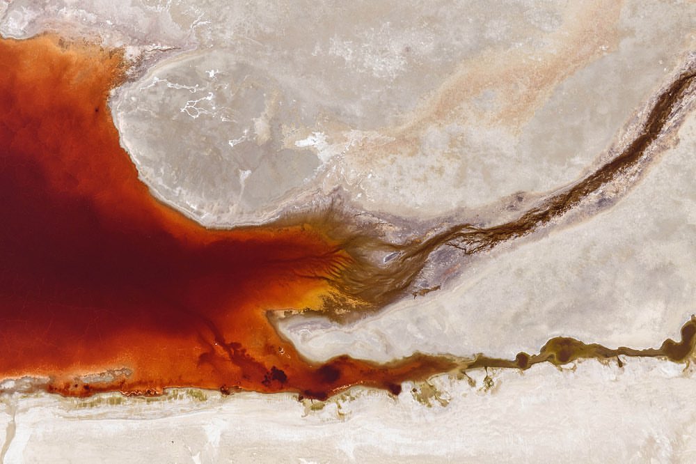 Aerial view of a red river or lake merging into the shoreline, creating a pattern of textures and colors in a natural landscape.