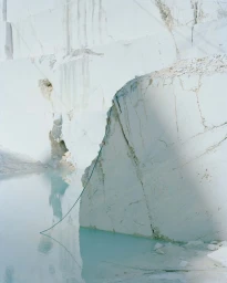 Large white marble quarry wall with a turquoise water pool and a hanging green rope photographed by Nick Meek
