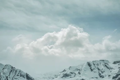 Snow-covered mountain peaks under a vast overcast sky with soft white clouds photographed by Nick Meek in Paris.