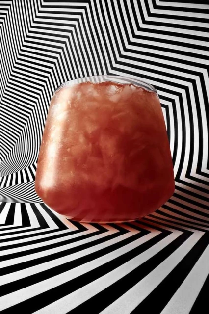 A refreshing drink with ice fills a clear glass against a graphic black and white striped background, creating a visually striking composition.