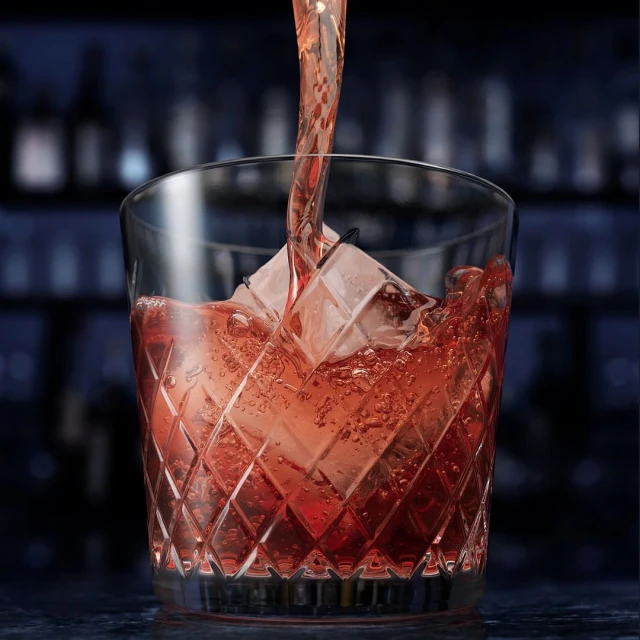 Crystal-cut glass filled with red liquid and ice, showcasing a drink with a focus on texture and color against a blurred background.