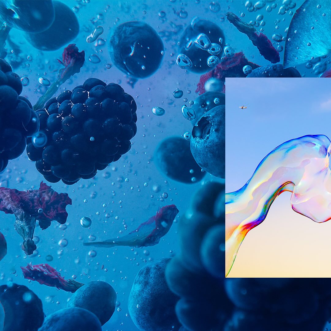 Macro studio shot of fresh blackberries and blueberries in water with air bubbles and rainbow color spectrum shapes against a blue sky.