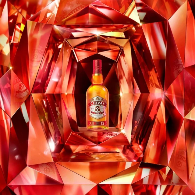 Chivas Regal 12 bottle prominently displayed against a red and copper geometric background, highlighting the whisky's branding.