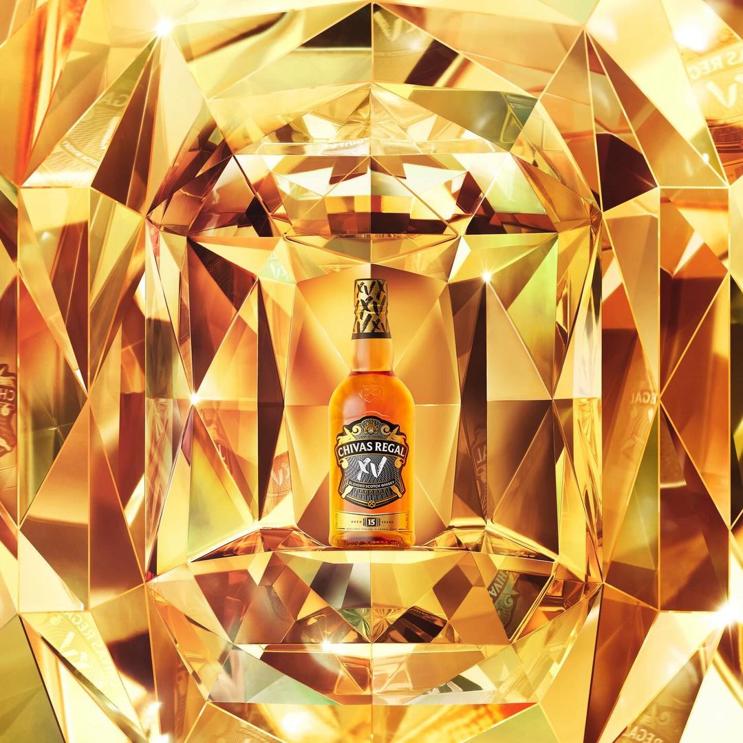 Chivas Regal whisky bottle stands out against a golden geometric backdrop, highlighting its premium branding in a studio shot.