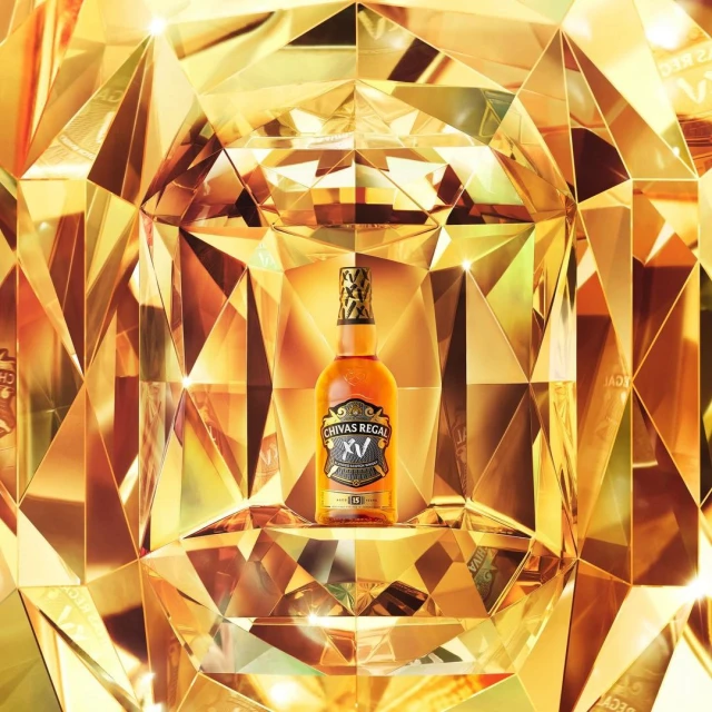 Chivas Regal whisky bottle stands out against a golden geometric backdrop, highlighting its premium branding in a studio shot.