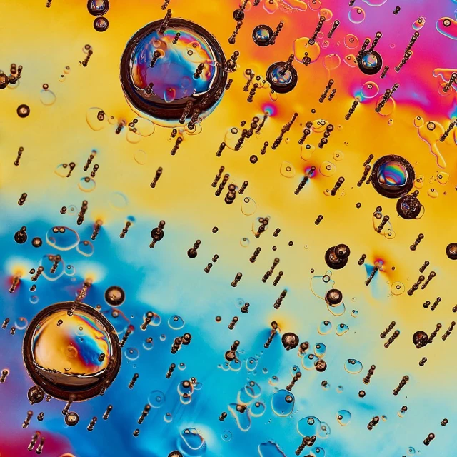Abstract close-up featuring large and small water droplets against a dynamic backdrop of pink, yellow, and blue gradients.