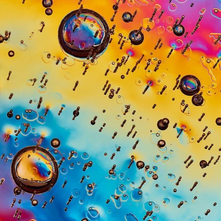 Abstract close-up featuring large and small water droplets against a dynamic backdrop of pink, yellow, and blue gradients.