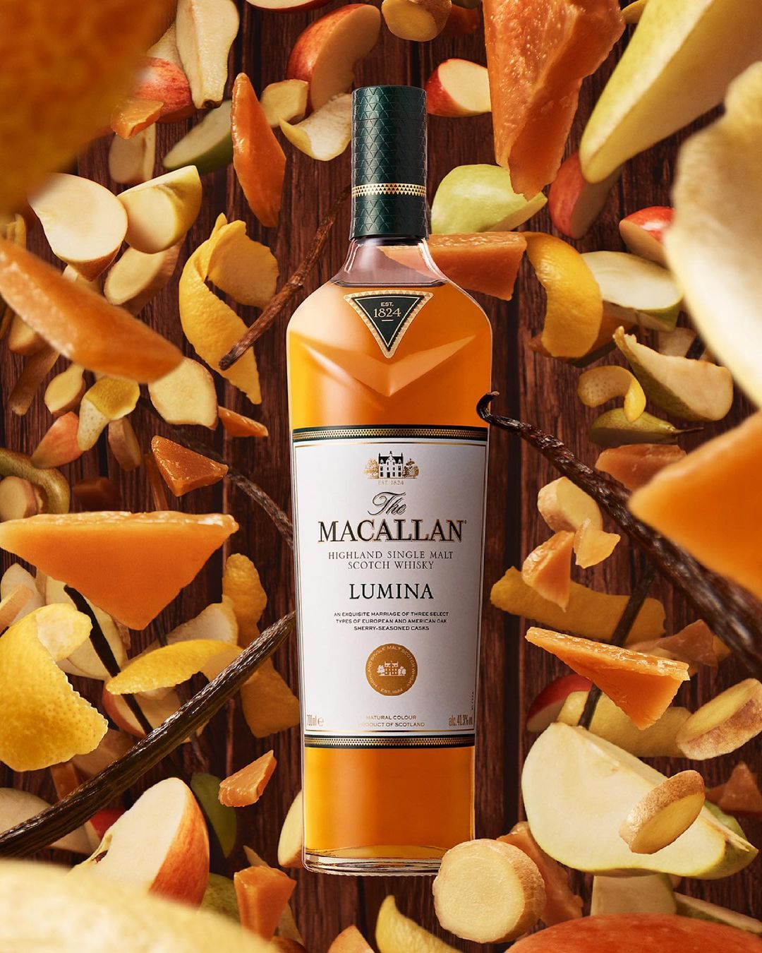 Bottle of Macallan Lumina scotch whisky on a dark wood surface, surrounded by floating slices of apples, pears, and citrus peels.