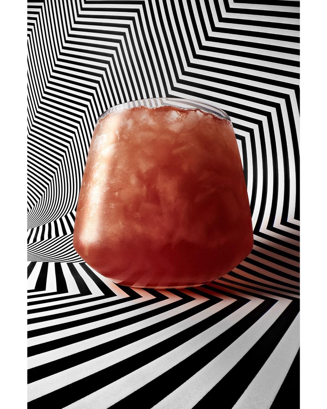 A glass filled with a pink beverage and ice is prominently displayed against a geometric black and white background, creating a modern aesthetic.