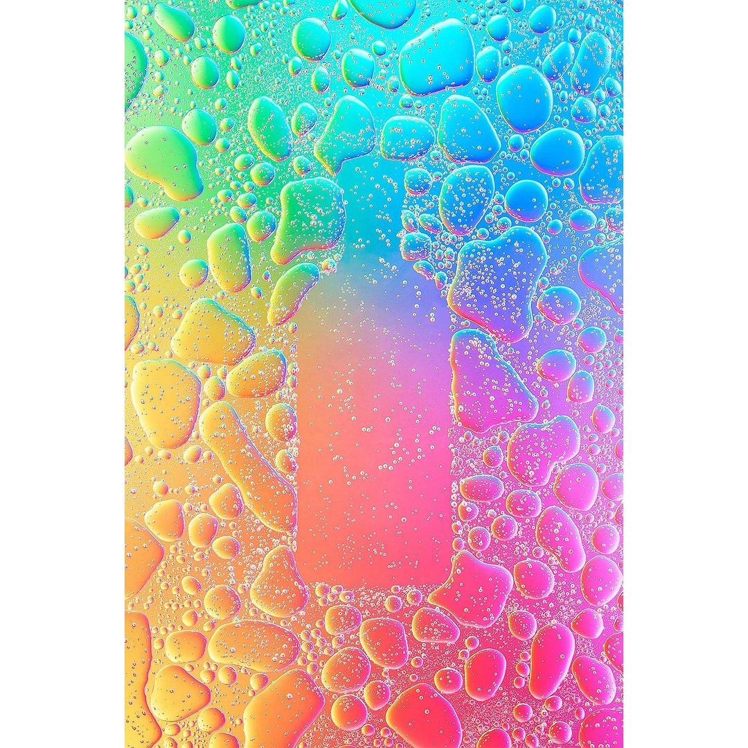 Abstract macro photograph featuring colorful water droplets and oil creating a rainbow effect, with a bottle shape in the center.