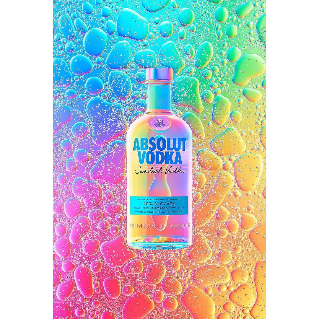 A bottle of Absolut Vodka stands out against a vibrant background of water droplets reflecting rainbow colors.  Studio shot.