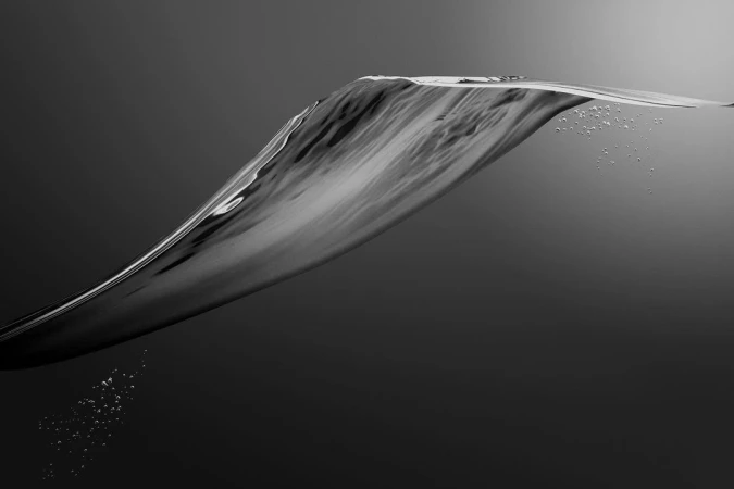Monochrome high-speed photograph of a dynamic water wave frozen in motion against a dark grey gradient background.