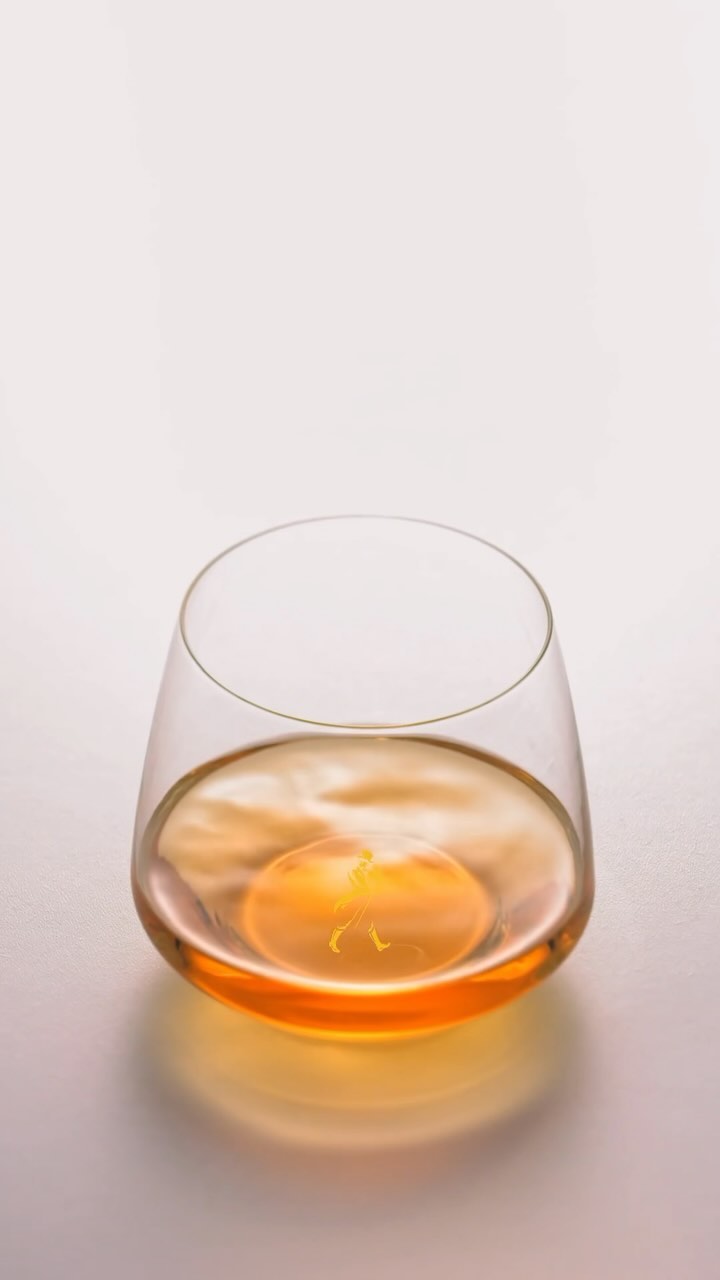 Stemless glass filled with amber liquid, featuring a smooth surface reflecting the light, all set against a plain backdrop.