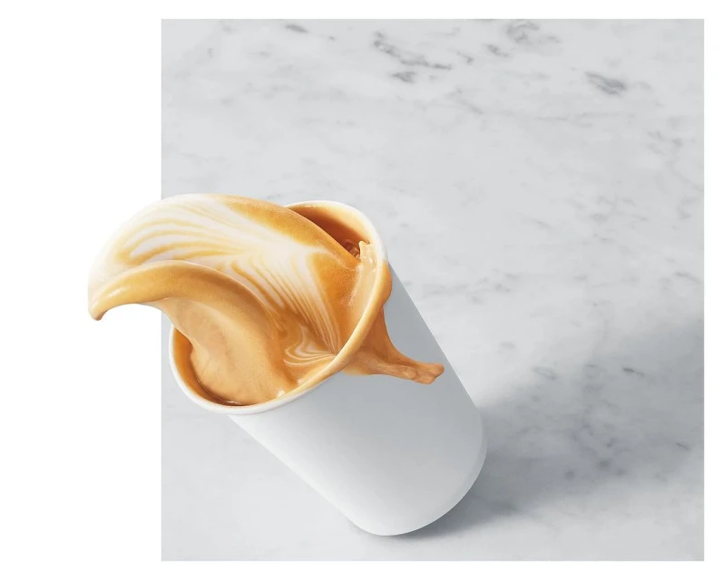 Coffee drink in a white cup with dynamic splash of liquid, set against a modern, minimalistic marble backdrop, creating a food and beverage image.