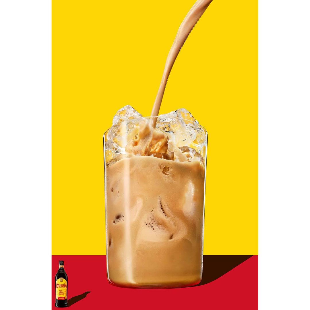 Iced coffee drink in glass on red and yellow background. Liquid is pouring into glass with ice, refreshing, caffeinated beverage.