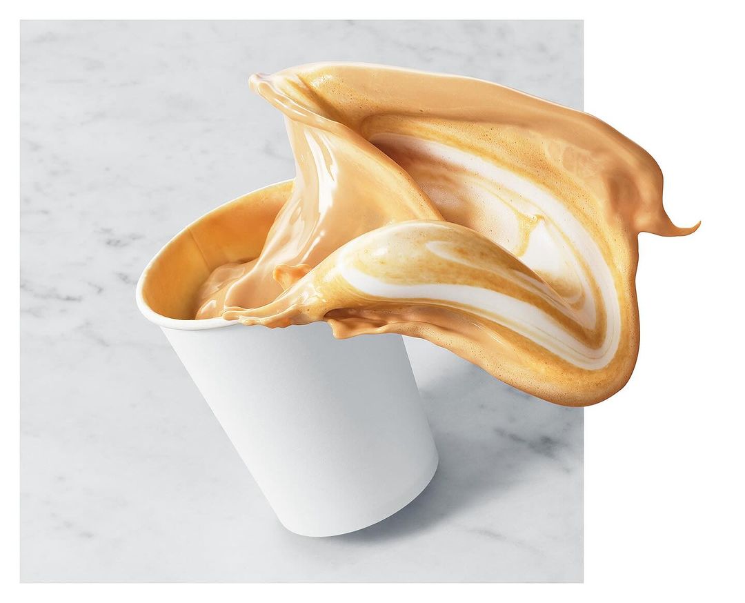 A cup with caramel-colored liquid is photographed close-up as it splashes, against a marble-like background with copy space on the right.