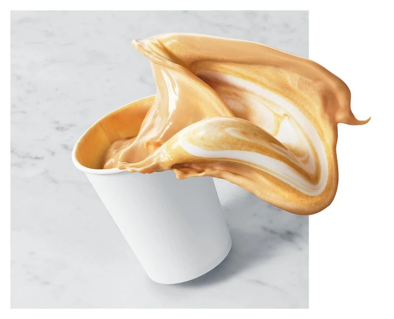 A cup with caramel-colored liquid is photographed close-up as it splashes, against a marble-like background with copy space on the right.
