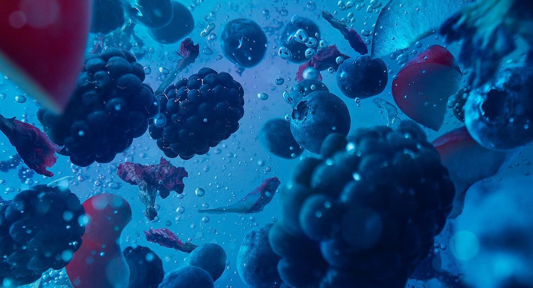 Close-up shot of blueberries, blackberries, and pieces of fruit floating in clear water with bubbles, creating a refreshing visual.