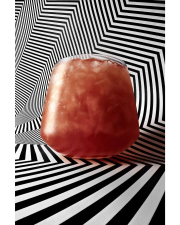 A stemless glass filled with a reddish brown iced beverage against a black and white geometric zigzag background.