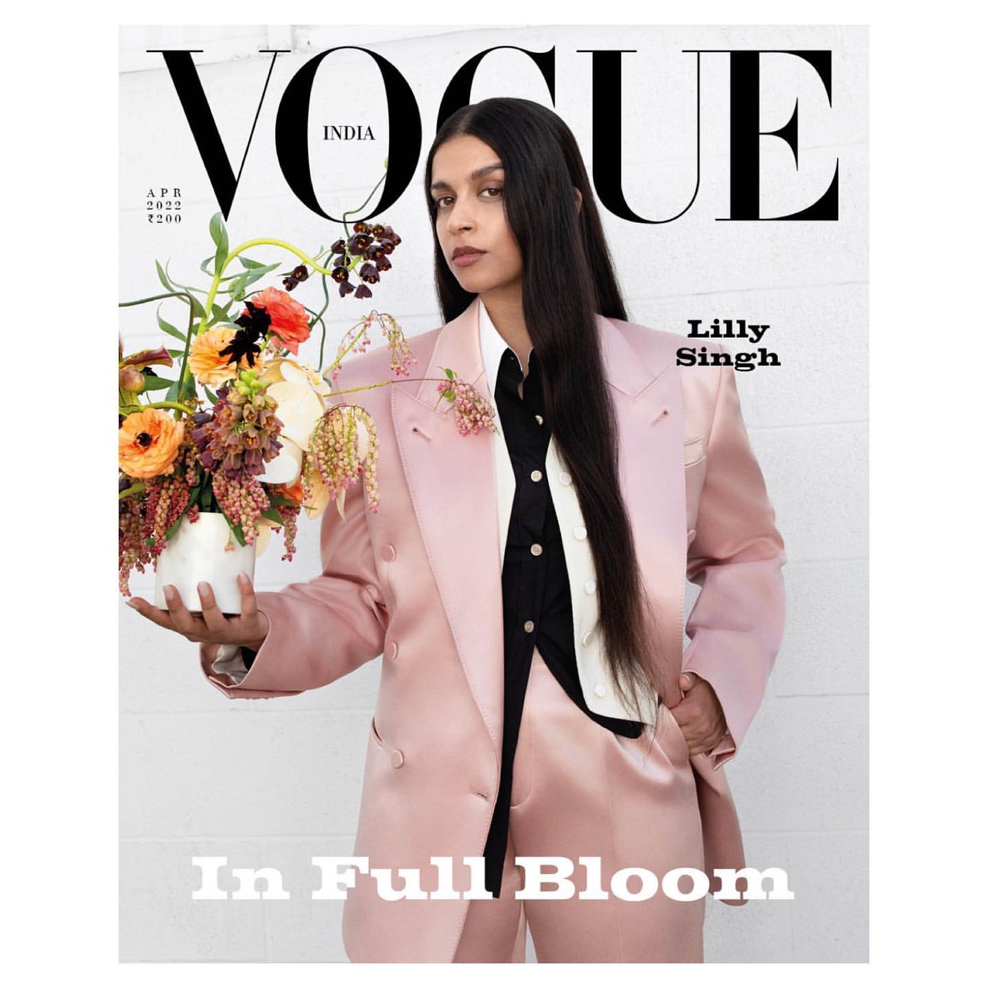 Vogue India cover featuring Lilly Singh wearing a pink suit and holding a bouquet of flowers in a white vase against a white wall.