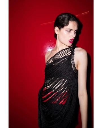Model wearing a black string top and vibrant pink lipstick against a bright red background in a vertical portrait photograph.