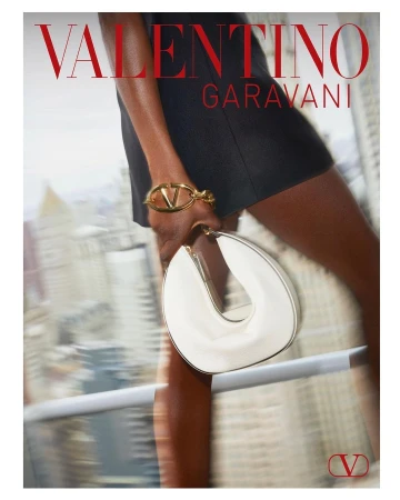 Close-up of a Black woman holding a white handbag and wearing a gold bracelet against an urban rooftop background by Nick Sethi