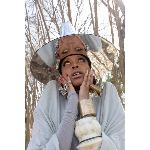 Portrait of an African-American woman with a silver hat looking up, wearing jewelry and light grey clothing in an outdoor setting.