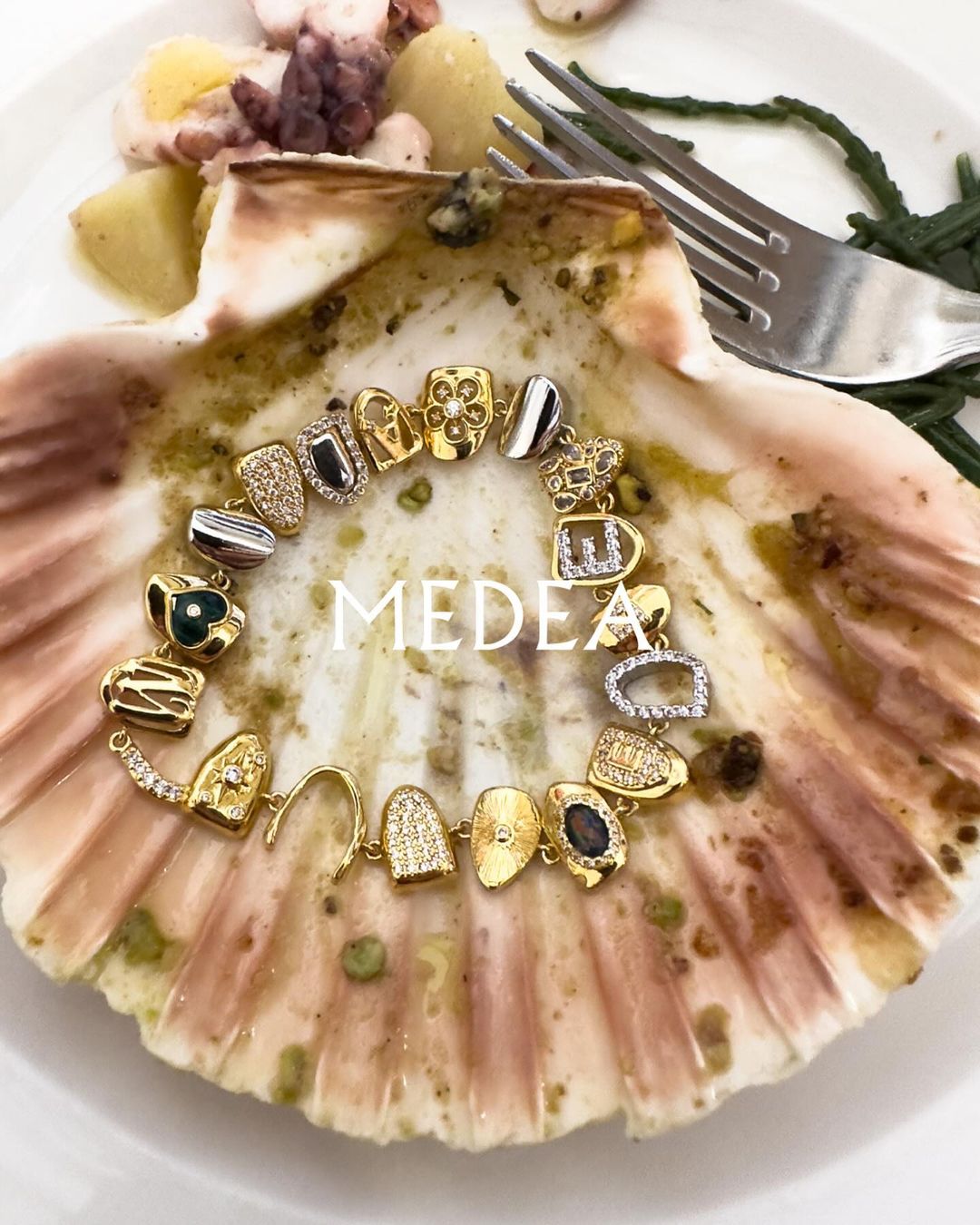 Gold charm bracelet featuring ornate gemstone and crystal pendants, displayed on a seashell with seafood, food and beverage concept.