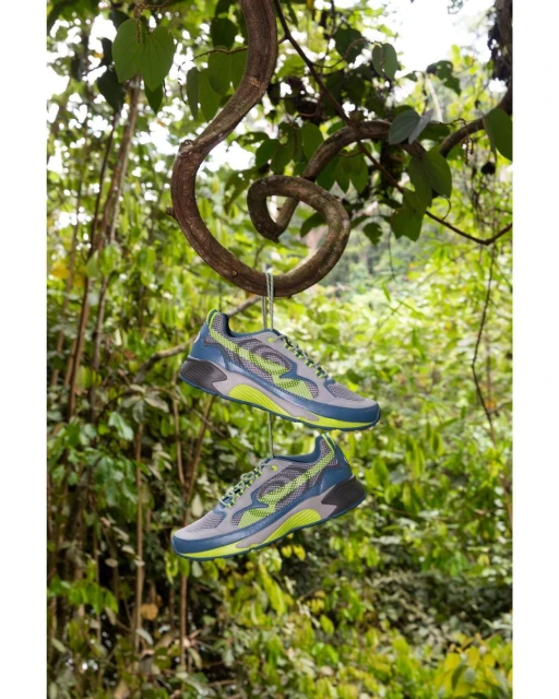 Two running shoes suspended by wire from a twisting vine in a lush outdoor setting with green foliage as the backdrop. Shoe product shot.