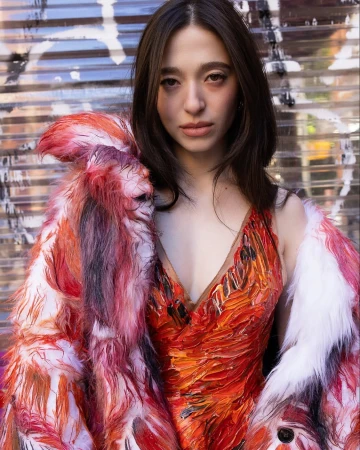 Portrait of a woman wearing a vibrant textured red dress and fuzzy patterned coat against a shutter door