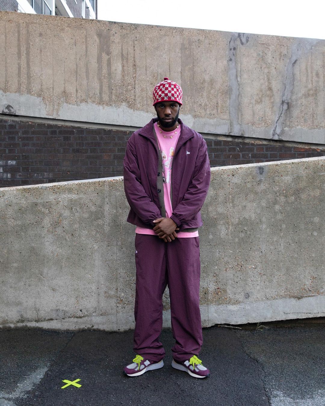 Adult male standing outside wearing a maroon jacket and matching pants with a pink T-shirt and checkered beanie.