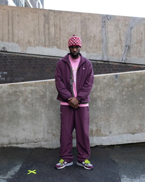 Adult male standing outside wearing a maroon jacket and matching pants with a pink T-shirt and checkered beanie.