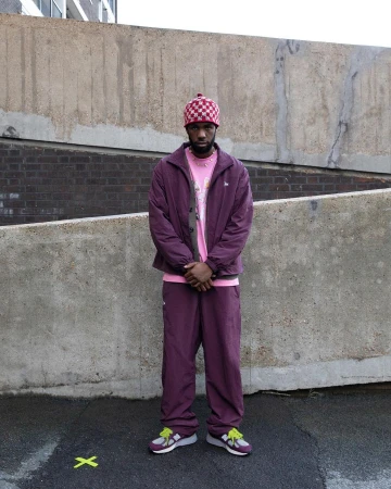 Adult male standing outside wearing a maroon jacket and matching pants with a pink T-shirt and checkered beanie.