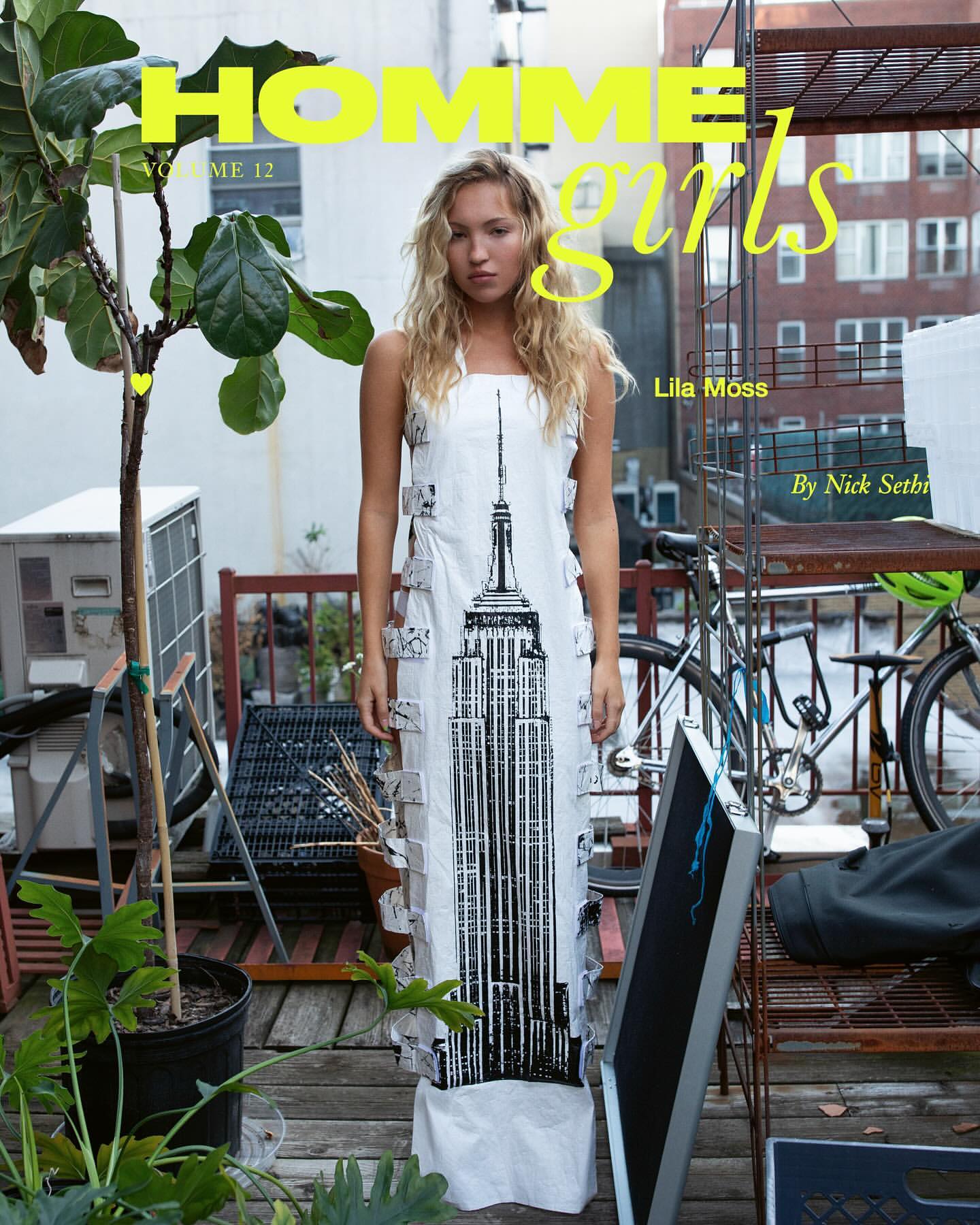 Fashion editorial featuring a woman in a dress with an Empire State Building graphic, plants, and bicycles in an outdoor setting.