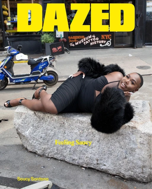 Magazine cover of Dazed featuring an adult posing on a stone, wearing a black dress and black faux fur shawl, with a blue scooter.
