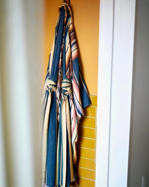 Striped robe hanging on a hook against a yellow tiled wall, next to a white door frame and white shower curtain.