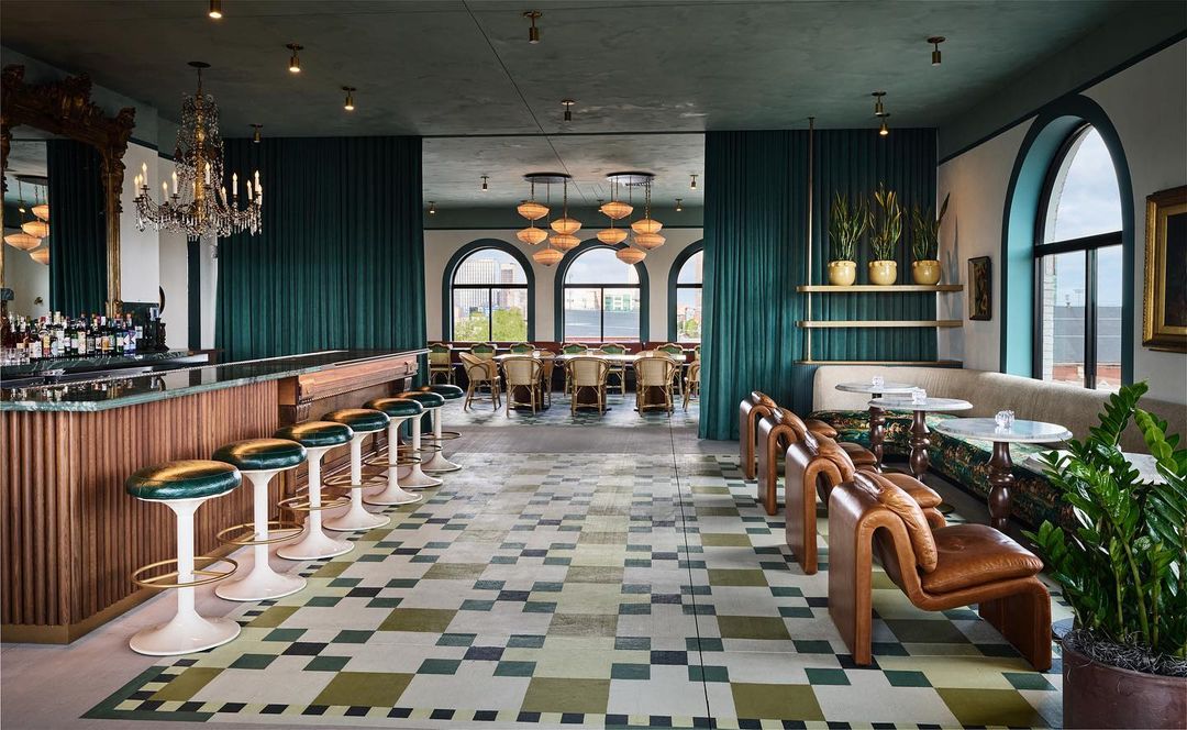 Elegant interior of a restaurant with bar, tables, and chairs. The patterned floor and chandeliers add visual interest.