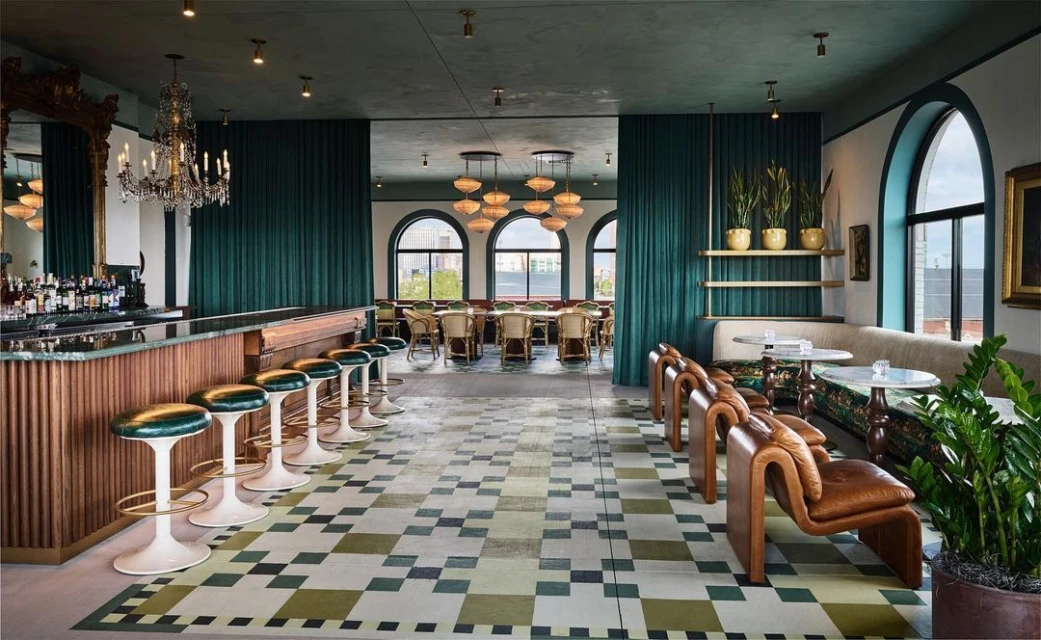 Elegant interior of a restaurant with bar, tables, and chairs. The patterned floor and chandeliers add visual interest.