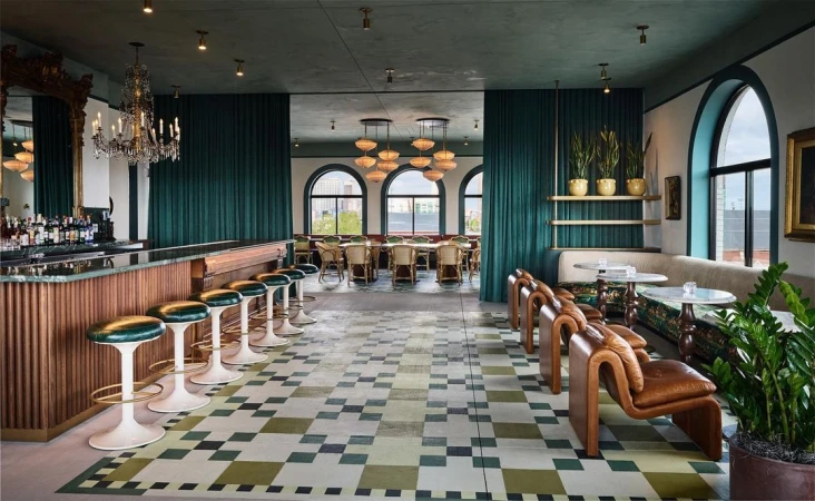 Elegant interior of a restaurant with bar, tables, and chairs. The patterned floor and chandeliers add visual interest.