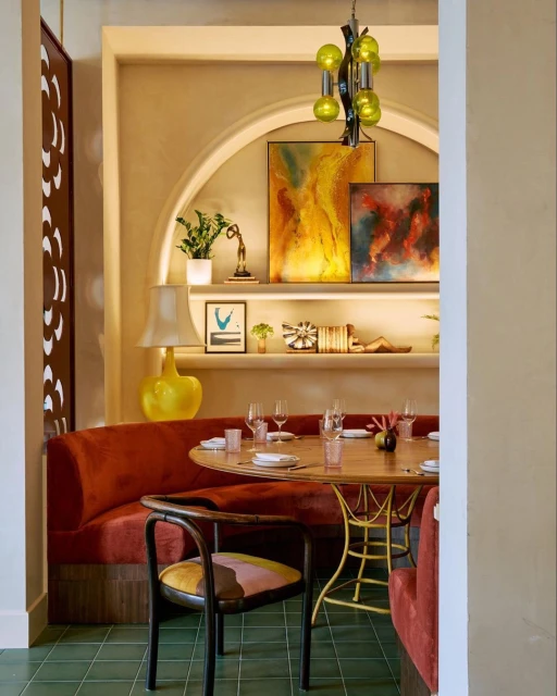 Interior of a restaurant with a rust-colored booth, round table set for dining, green tile floor, and decorative wall features.