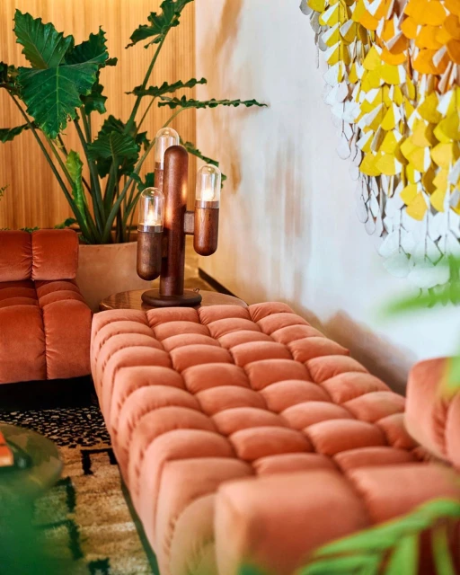 Living room with a coral-colored couch, wooden cactus lamp, and green plants in a modern interior setting, creating a cozy atmosphere.