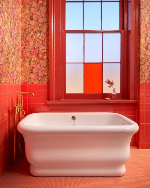 Elegant bathroom with a clawfoot tub, coral tiles, and floral wallpaper, bathed in natural light from a large window.