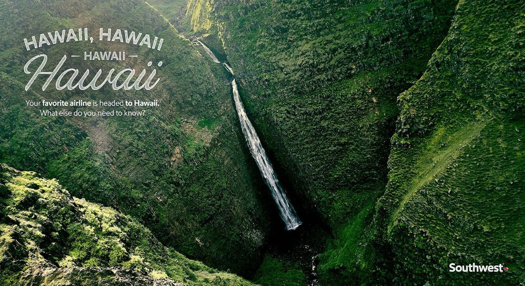 Scenic aerial view of a lush green valley with a striking waterfall cascading down its steep slopes in Hawaii, on a bright day.