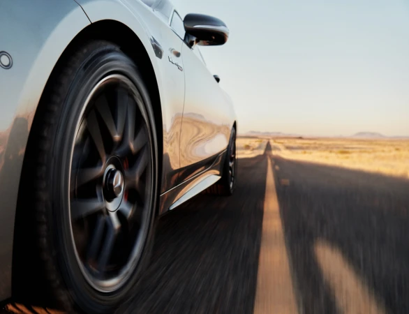 Silver car in motion on a highway with a desert landscape under a clear sky, showcasing speed and automotive design.